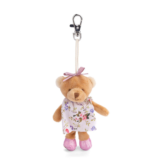 A brown teddy bear bag charm with a floral dress, pink bow, and pink shoes attached to a clip.