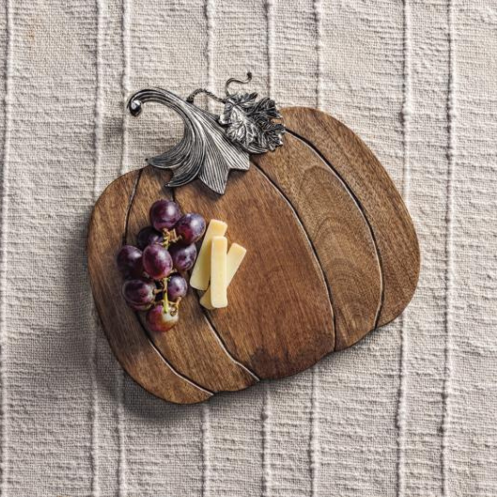 Wooden pumpkin-shaped board with grapes and cheese on a textured surface