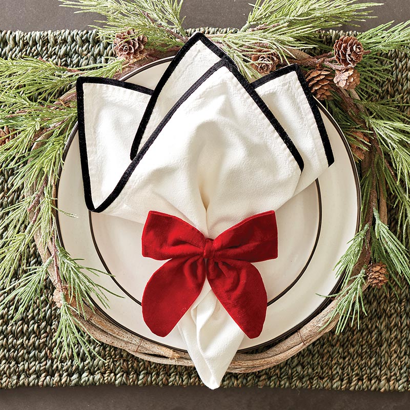 red velvet bow napkin tie displayed on a white napkin resting on a white plate surround by pine sprigs