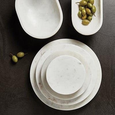 stack of marble boards on a dark brown table with a bowl of fruits.