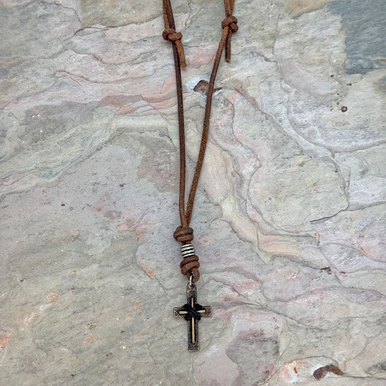 Aadi Cross Leather Necklace laying on a rock slab
