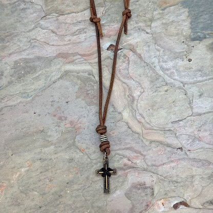 Aadi Cross Leather Necklace laying on a rock slab