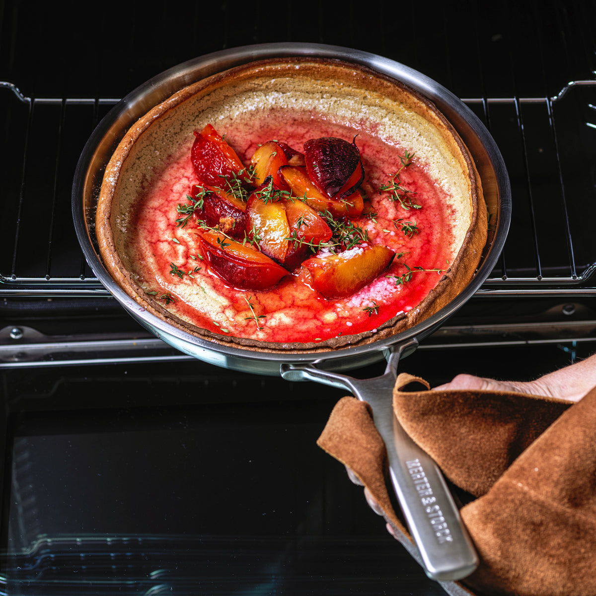 hand holding frypan filled with backed fruit dessert, pulling it out of the oven.