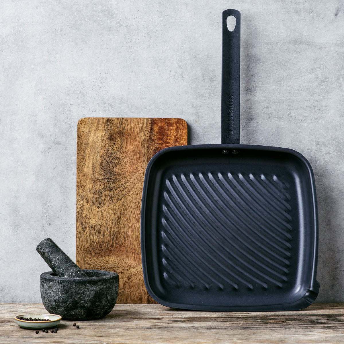 grill pan on wooden countertop standing on end, leaning against a wall with a cutting board behind it and a spice grinder in front of it.