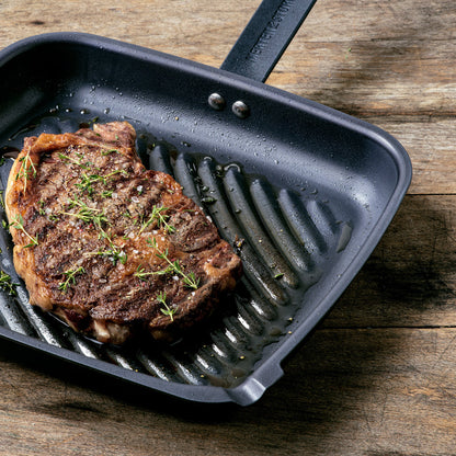 grill pan with a grilled piece of meat in it set on a wooden table.