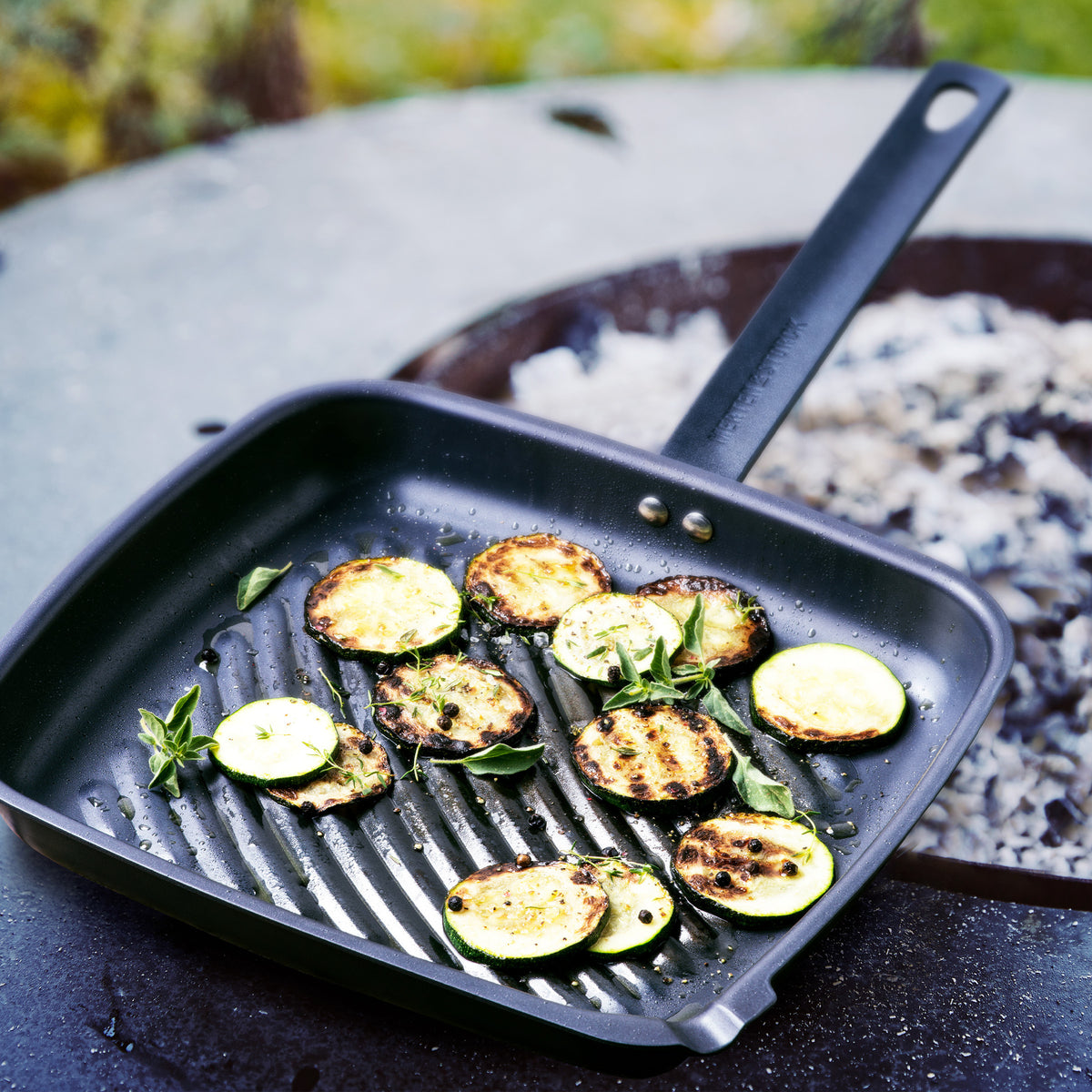 grill pan with grilled veggies in it set next to a fire.