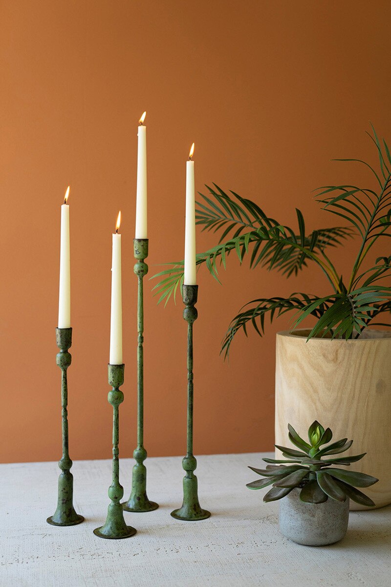 4 tall green candlesticks with white candles against an orange wall.