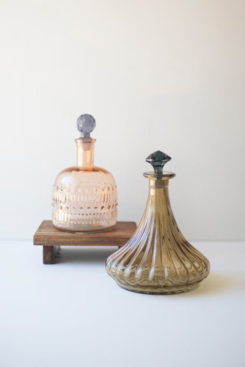 Two decorative glass decanters on a white surface with a light gray background