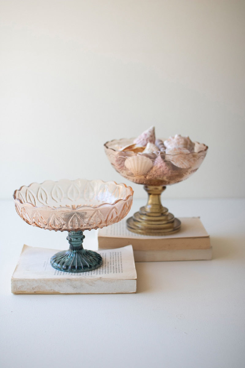 two glass compotes with blush colored bowls, one has blue pedestal, the other green