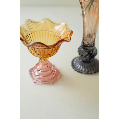 Amber glass footed bowl on a white surface with another glass item in the background.