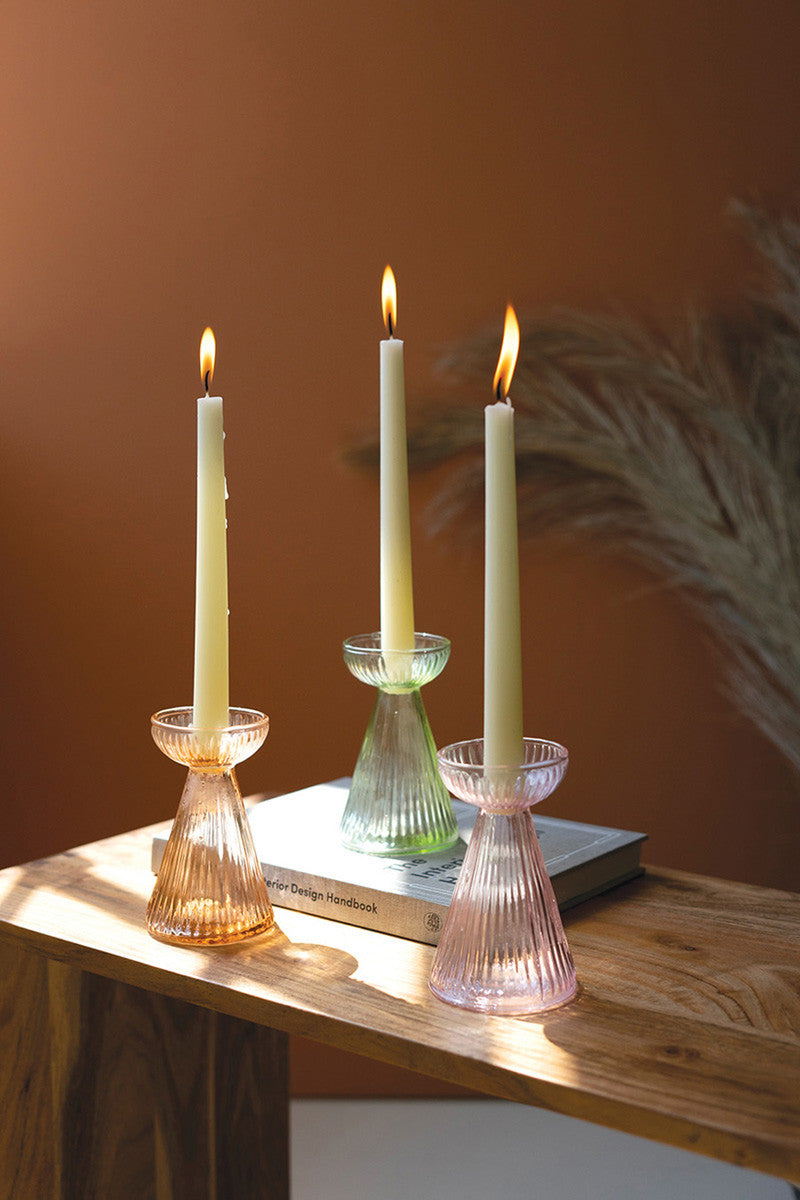3 colors of glass vases on a wooden table with lit taper candles in the.