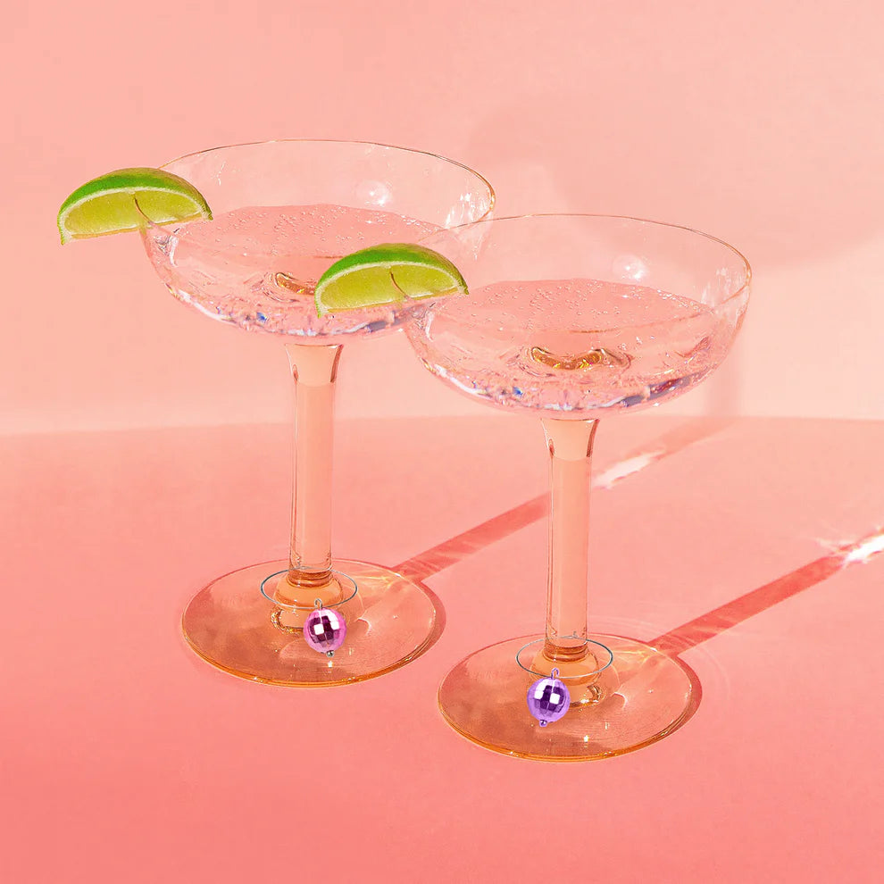 2 margarite glasses with lime wedges on the rims and disco ball drink markers on the stems.