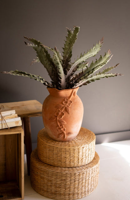 Terracotta vase with a plant in it on top of woven boxes against a neutral background