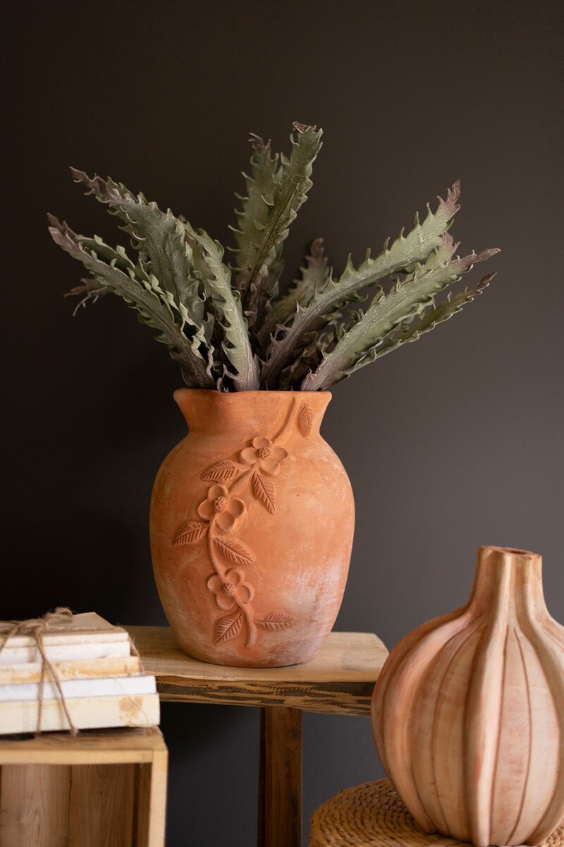 Terracotta vase with a plant in it on a wooden surface against a dark background