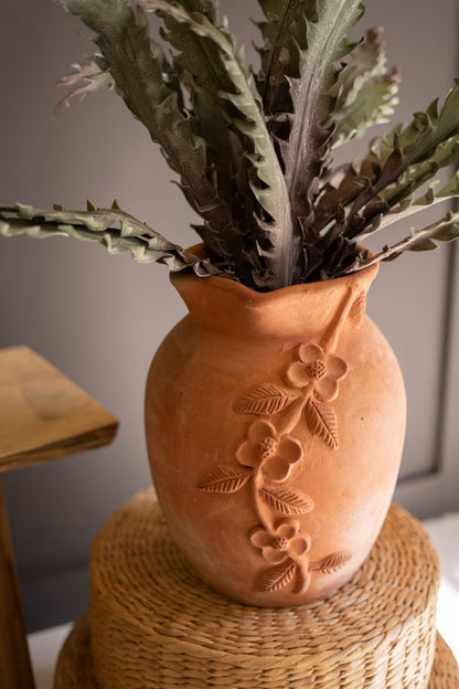 Terracotta vase with floral patterns on a woven surface