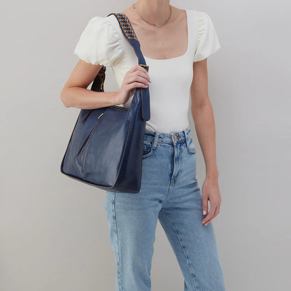person wearing jeans and a white top with navy bellamy bag on their shoulder.