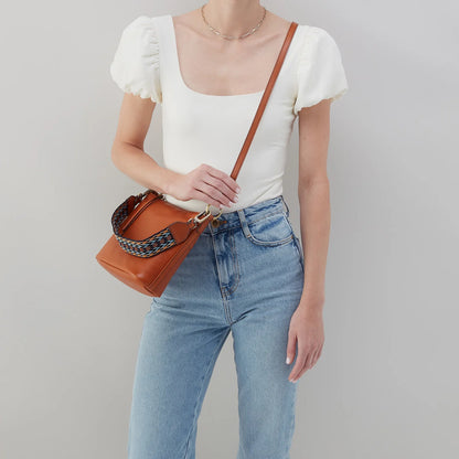 person wearing jeans and a white top with honey brown bell shoulder bag across their chest.