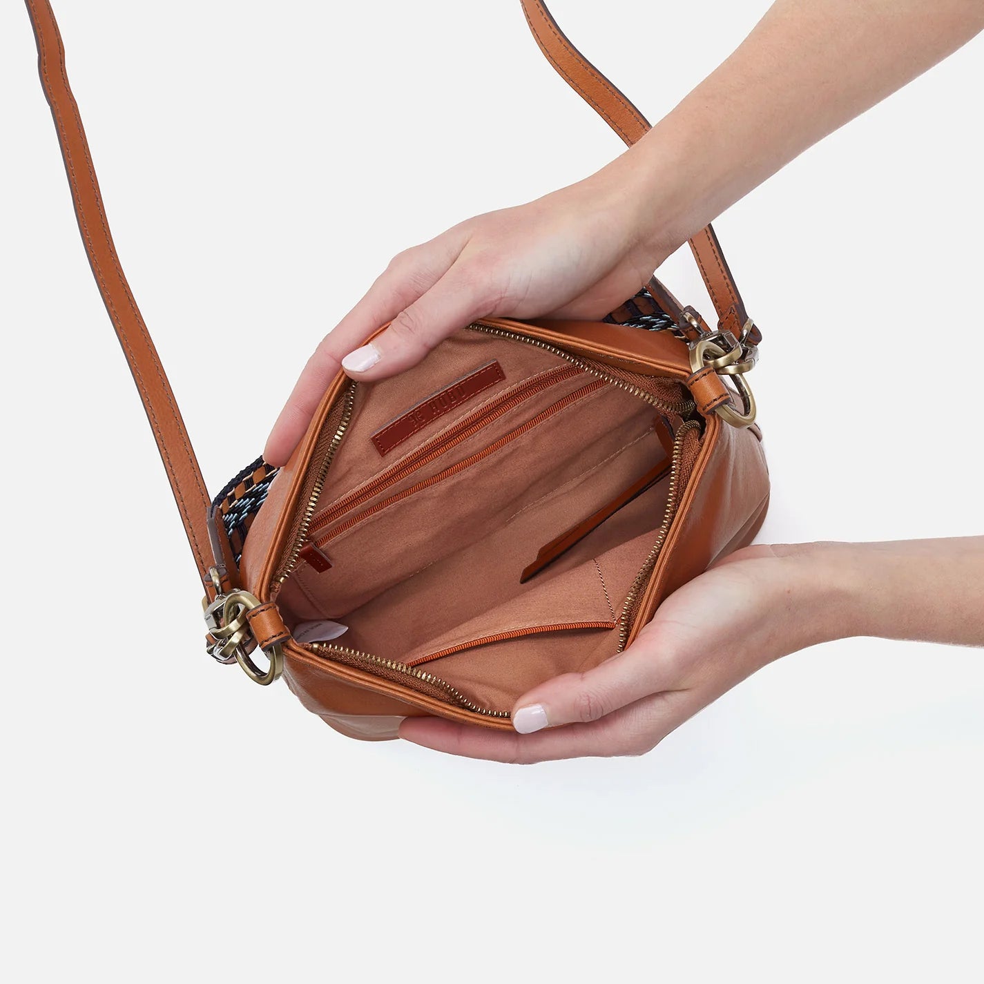 hands holding open honey brown bell shoulder bag showing interior.