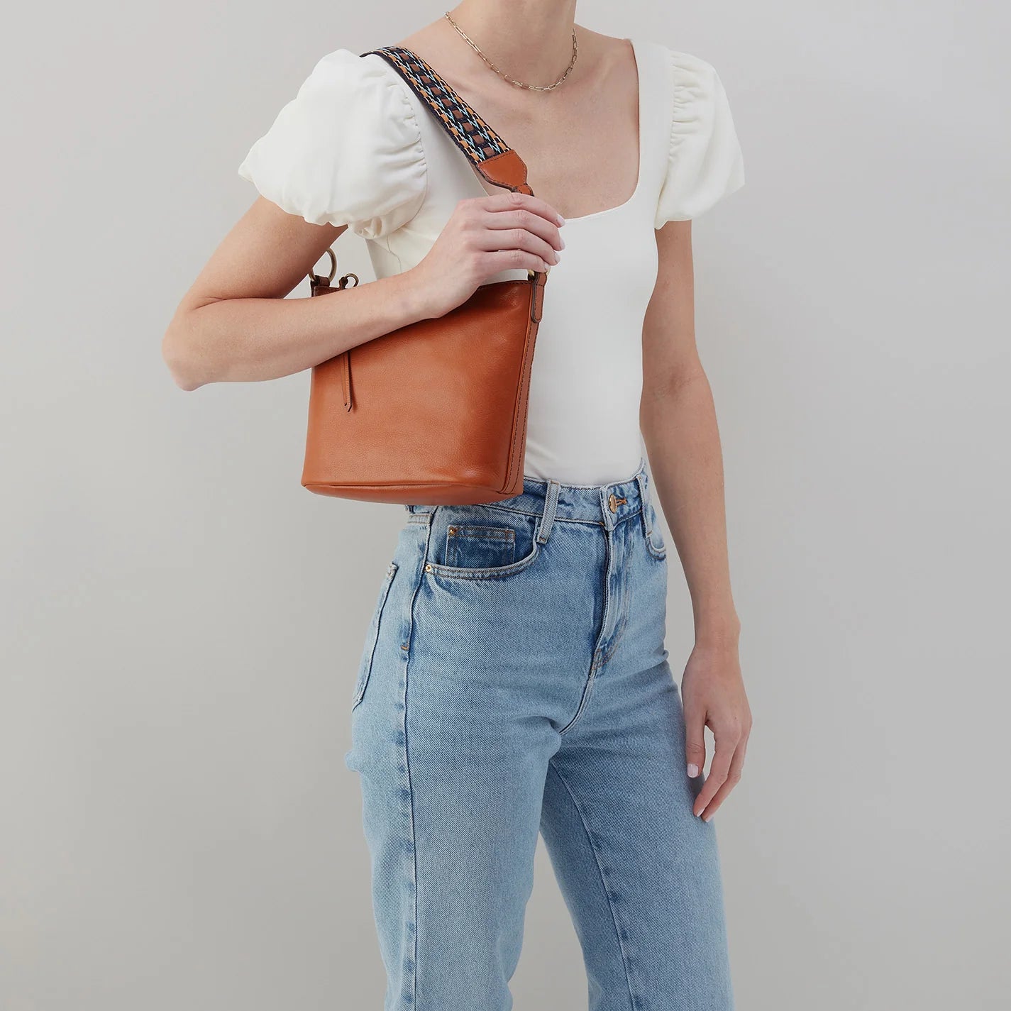 person wearing jeans and a white top with honey brown bell shoulder bag on their shoulder.