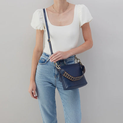 person wearing jeans and a white top with navy bell shoulder bag across their chest.