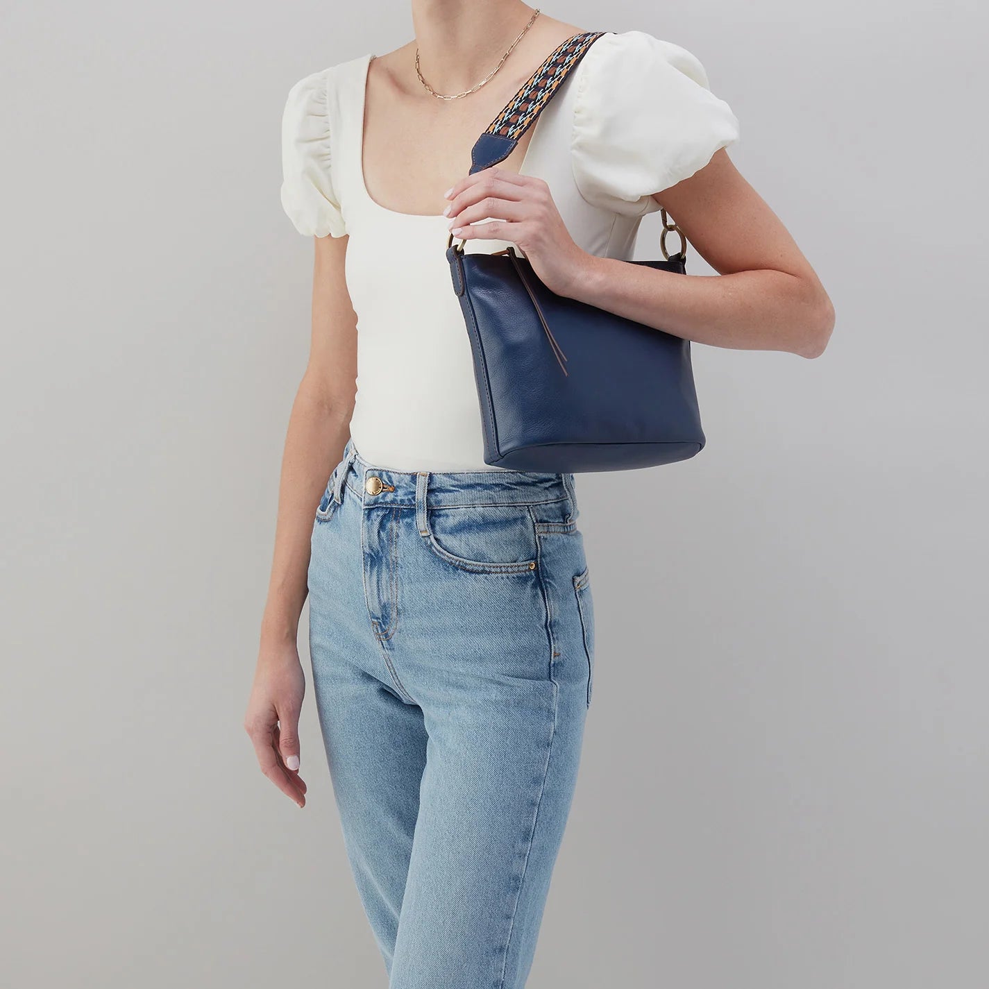 person wearing jeans and a white top with navy bell shoulder bag on their shoulder.