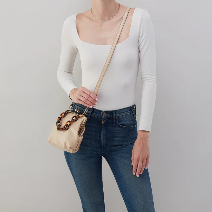 person wearing jeans and a white top with quartz alba purse with a tortoise chain handle and crossbody strap over their shoulder.