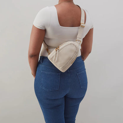 person wearing jeans and a white top with birch fern sling bag on their back