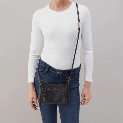 Person wearing jeans and a white top with black Darcy crossbody With studded floral design across their shoulders