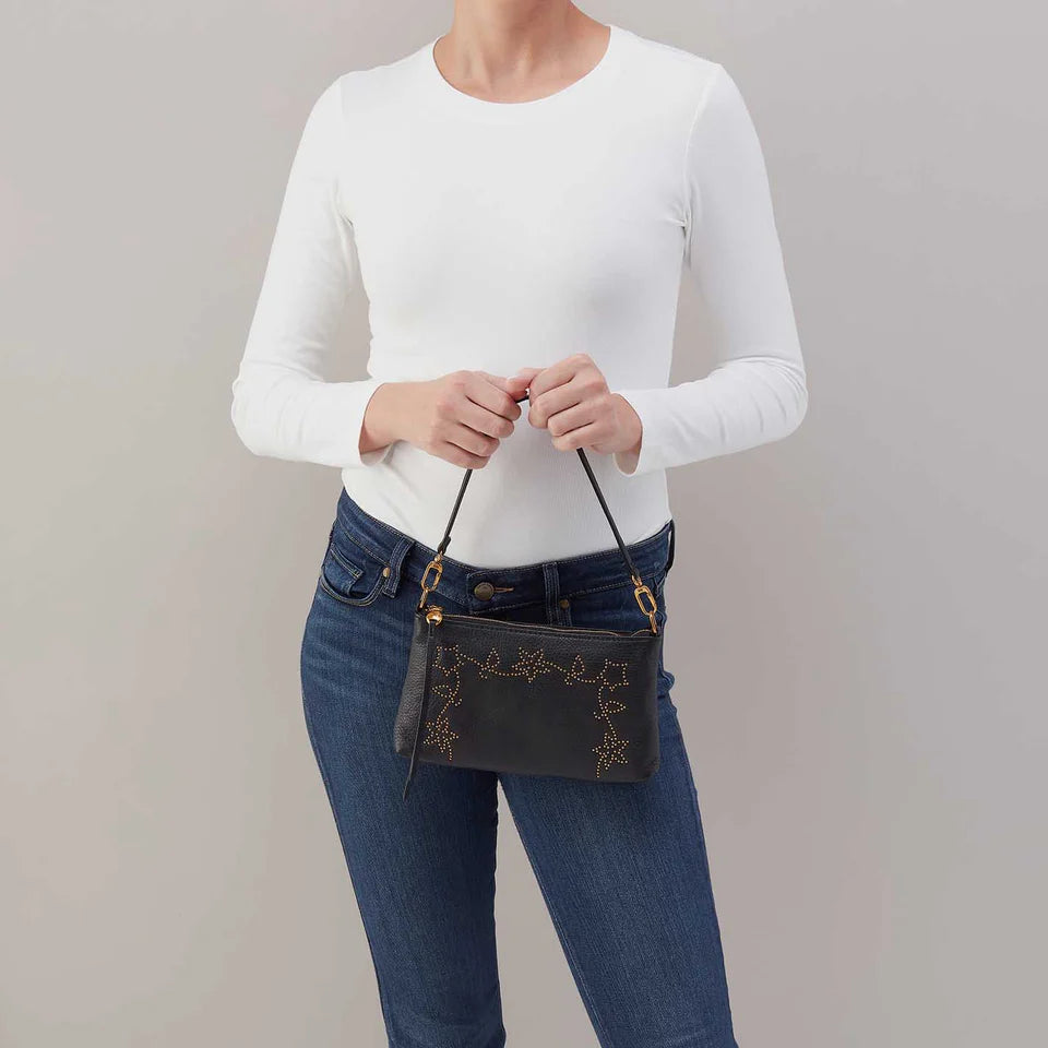 Person wearing jeans and a white top carrying Darcy crossbody with studded floral design by the small shoulder strap