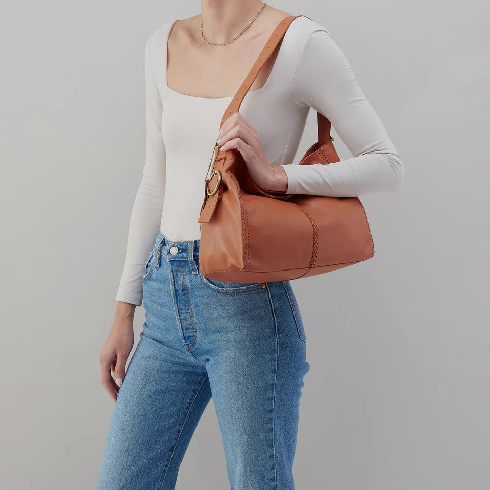 person wearing jeans and a white top with a Brown leather handbag with braided trim on their shoulder