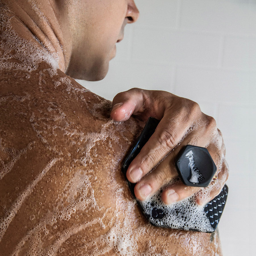 person covered with bubbles using scrubber to wash shoulder