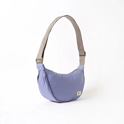 angled view of lavender shoulder bag with crescent shape and grey strap shown on a white background