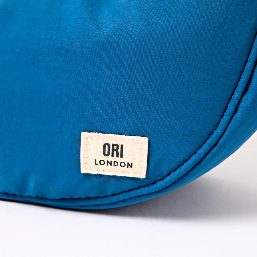 close-up of botton corner of Blue bag with an 'ORI London' label on a white background