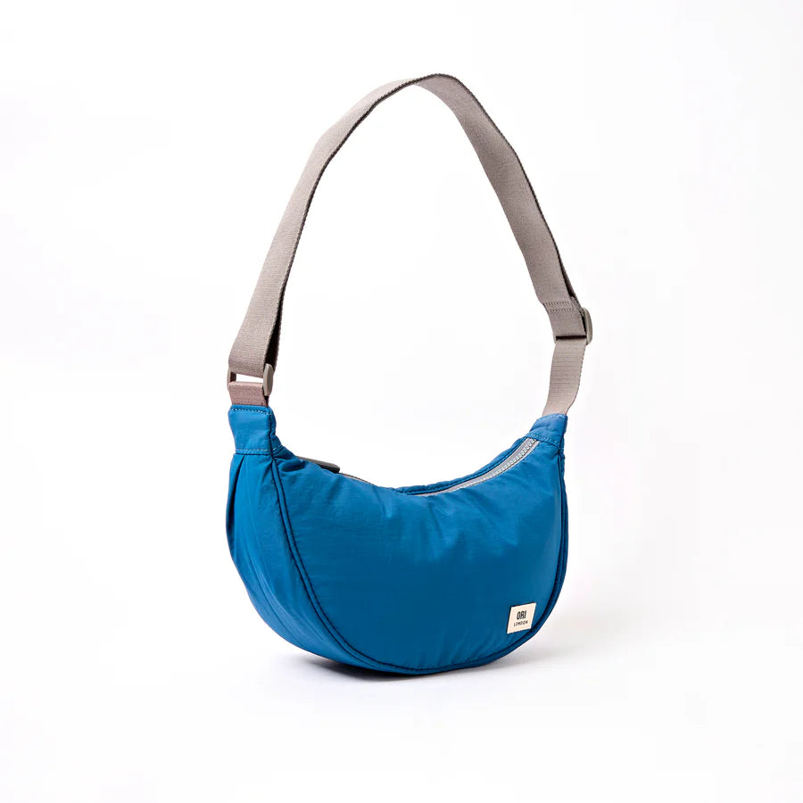 angled view of bright Blue handbag with a gray strap on a white background