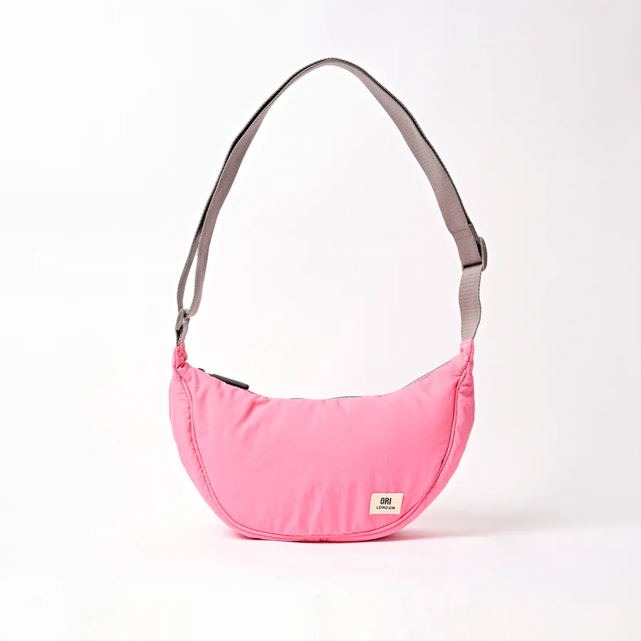 pink shoulder bag with crescent shape and light grey strap shown on a white background