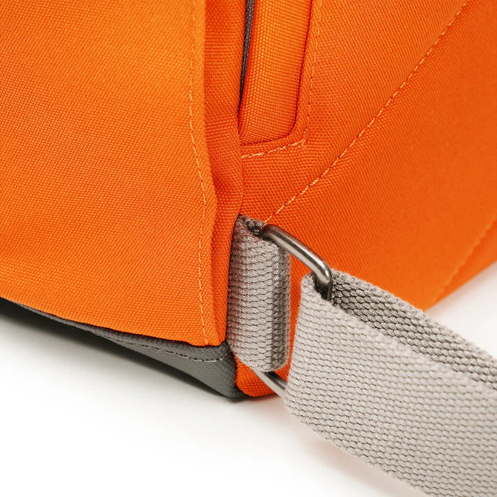 Close up of strap attachment on bottom corner of orange backpack.