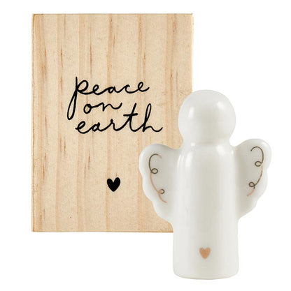 white angel with gold accents on its wings and a small heart on the bottom set next to a wooden box.