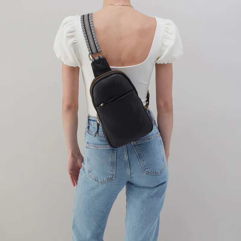 person wearing jeans and a white top with black cass sling bag on their back.