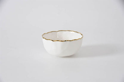 White ceramic bowl with gold rim on a light gray background