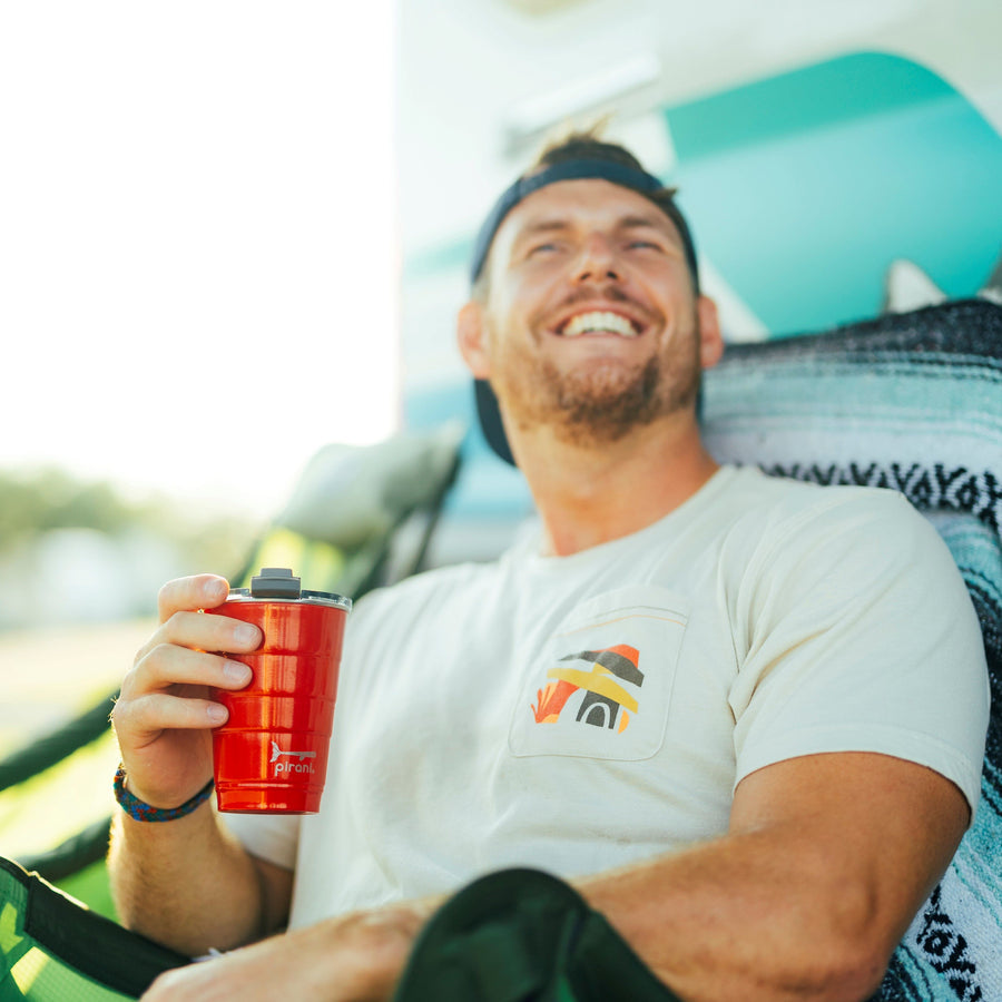 guy with big smile lounging with a red tumbler.