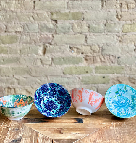 4 assorted colorful bowls arranged on a table in a row on a wood table with a brick wall background.