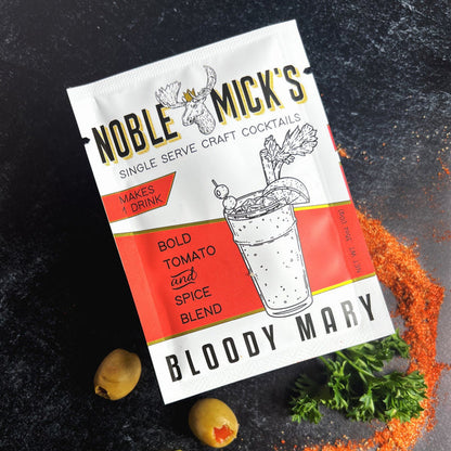 noble mick's single serve packet of bloody mary mix on a bar top with spices and olives.