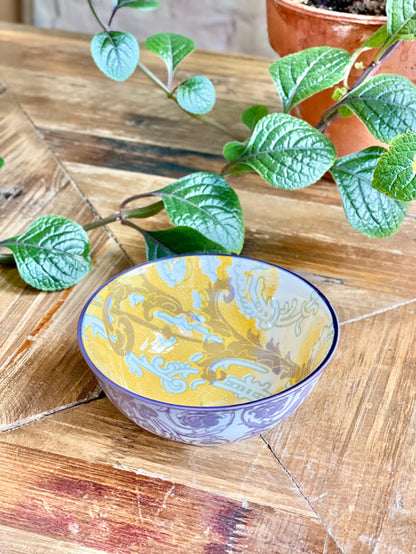 yellow and purple small bowl with artistic pattern on a wooden table with greenery.