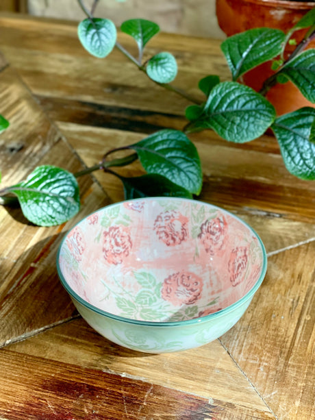 pink and green small bowl with artistic pattern on a wooden table with greenery.