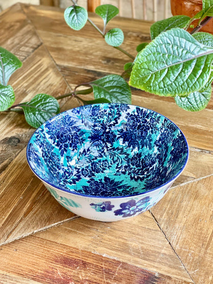 blue and torquoise  bowl with an artistic pattern on a wooden table with greenery.