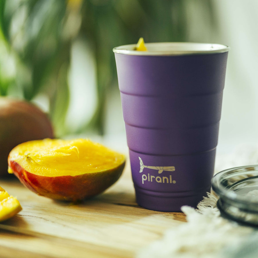 purple tumbler on a table with a sliced fruit next to it.