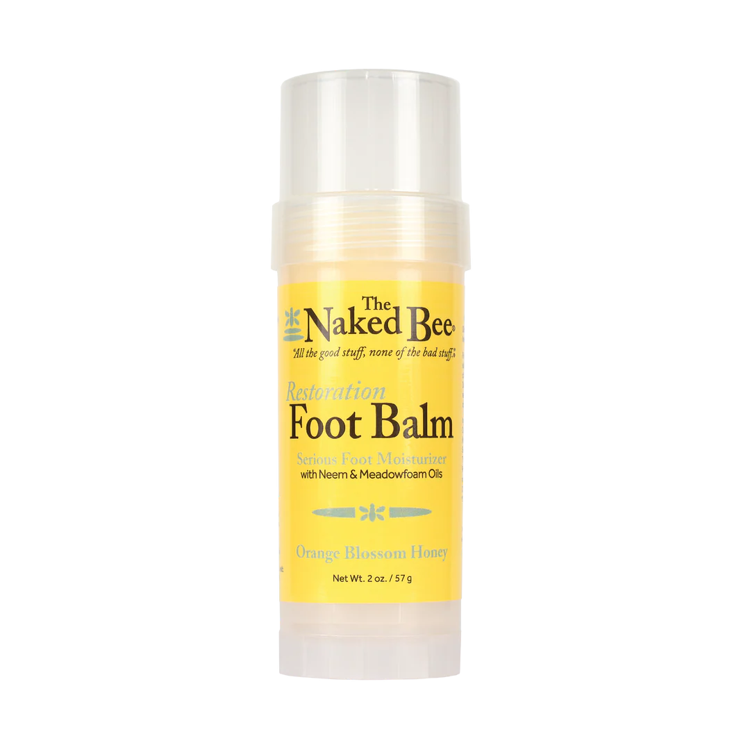 The Naked Bee Restoration Foot Balm stick in Orange Blossom Honey scent, featuring a yellow label and clear plastic cap and base, on a white background.