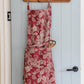 ruby fig apron hanging on wooden hooks on a white slat wall.