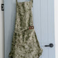 olive green fig apron hanging on wooden hooks on a white slat wall.