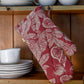 ruby oven mitt hanging on a wooden cabinet filled with white dishes.